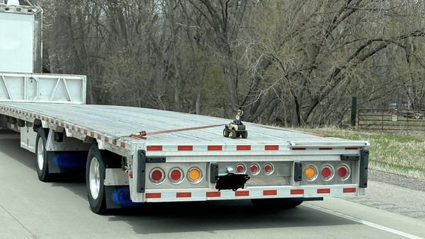 A toy Woody figure rides alone on the back of a flatbed trailer
