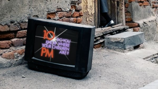 A CRT television sits in an alley, its screen reading “10 PM Do you know where your children are?”