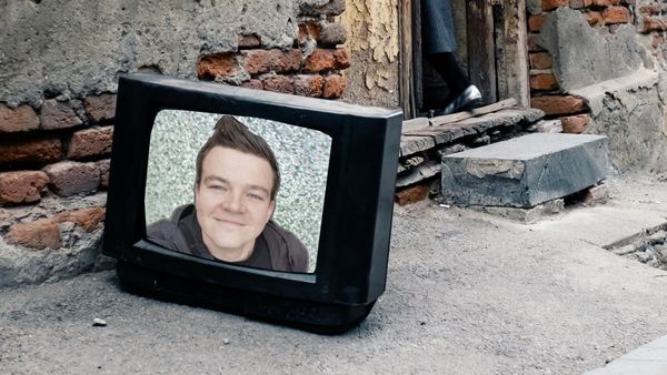 A smiling young man appears on the television screen through the static